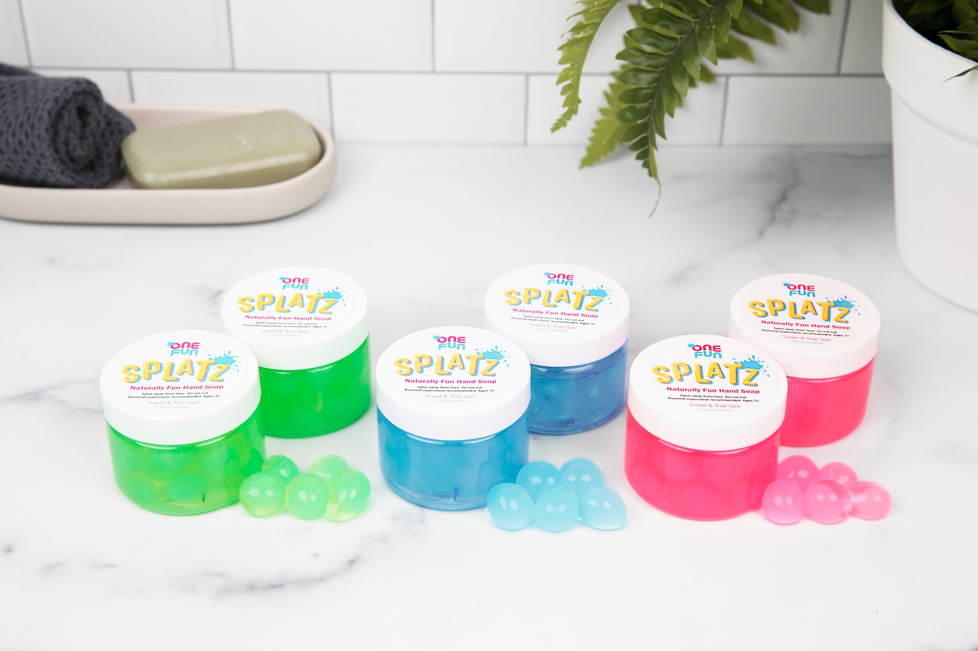 On a bathroom counter. Two 3oz jars of green bursting soap bubbles, two 3oz jars of turquoise bursting soap bubbles, and two 3oz jars of pink bursting soap bubbles
